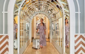A guest pulls a silver suitcase through a grand mirrored arched hallway at a boutique hotel in Los Angeles.