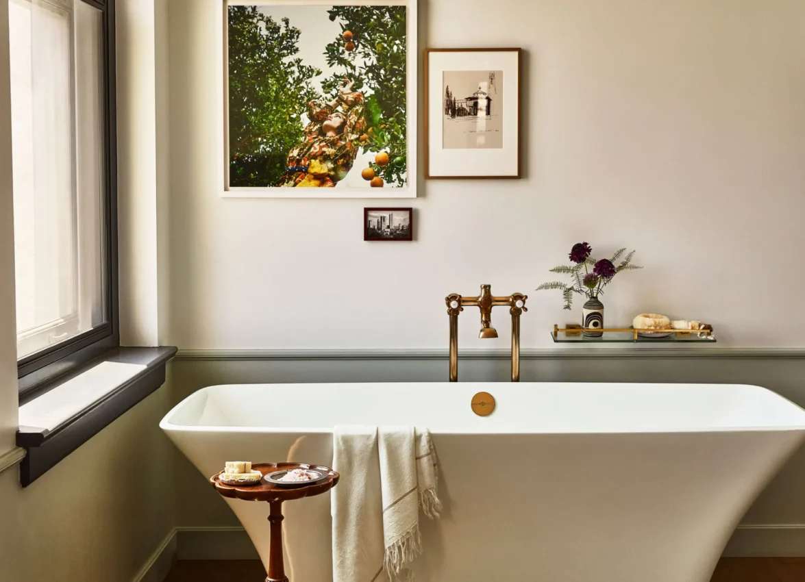 A freestanding white soaking tub with brass hardware and artwork in a luxury hotel suite at Hotel Per La.