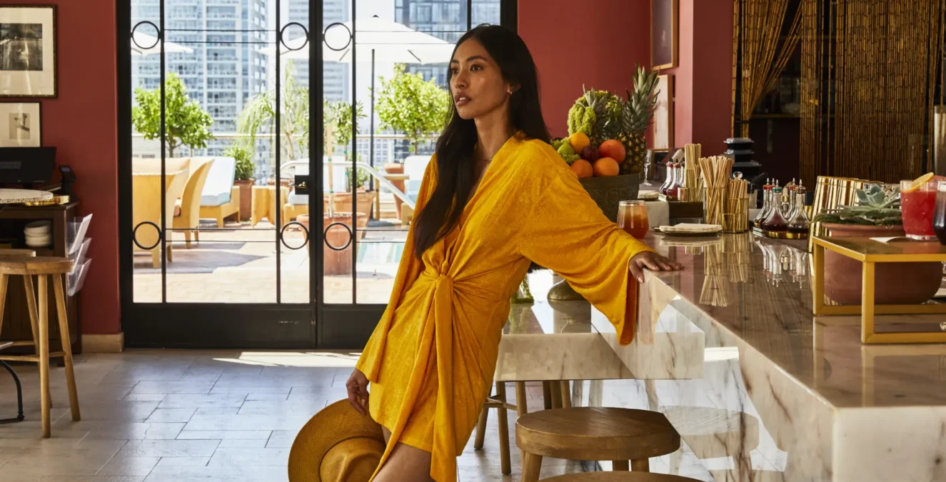 A woman in a yellow dress leans against the marble counter at Bar Clara, a stylish rooftop bar in Los Angeles.
