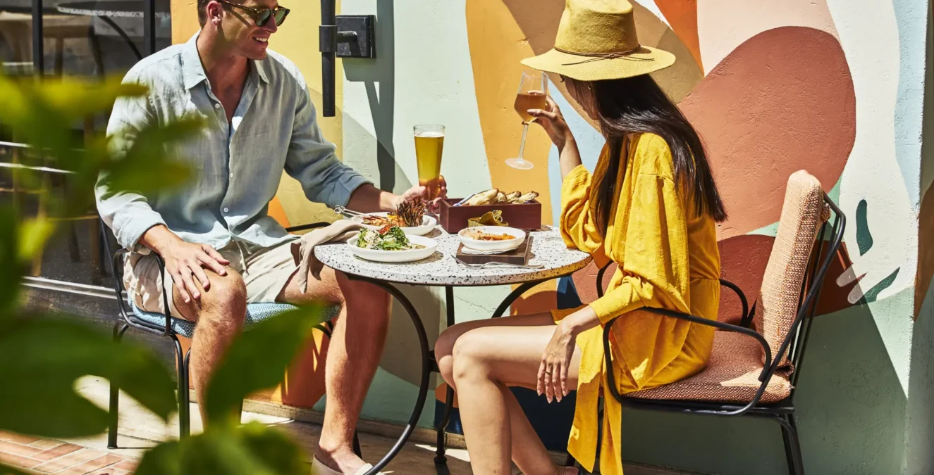 A couple enjoys drinks and appetizers at Bar Clara, a vibrant rooftop bar in Los Angeles with colorful wall murals.