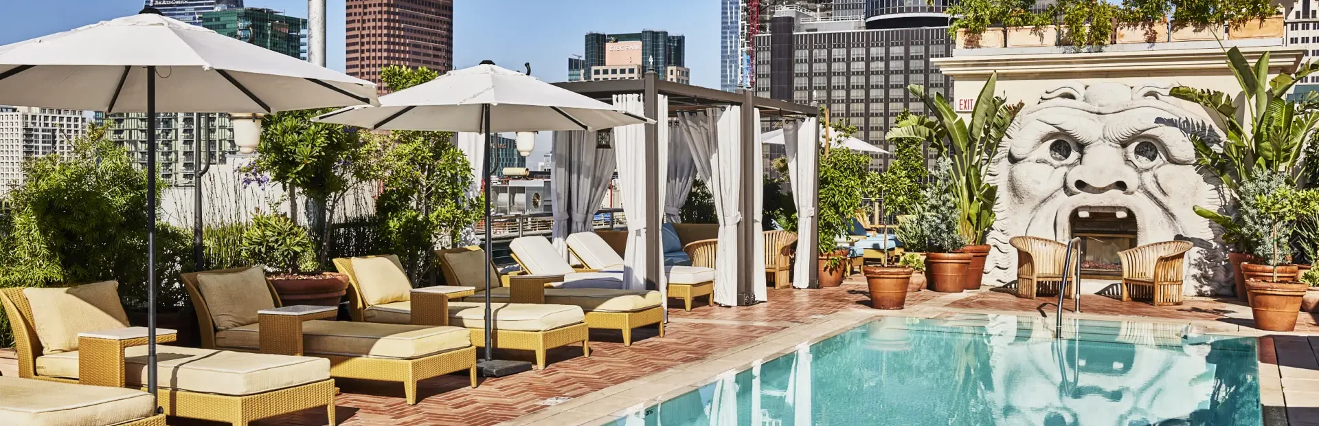 Guests enjoy the Bar Clara rooftop pool hotel Los Angeles deck featuring plush loungers and a carved stone facade.