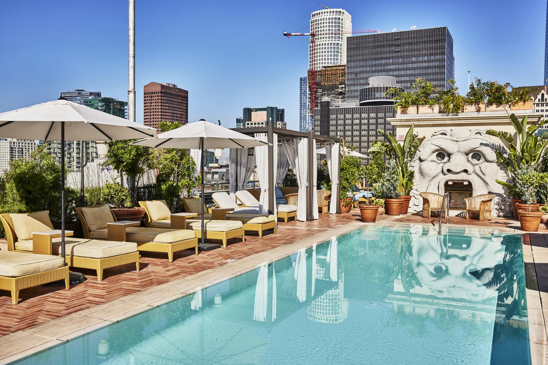 Guests enjoy the Bar Clara rooftop pool hotel Los Angeles deck featuring plush loungers and a carved stone facade.