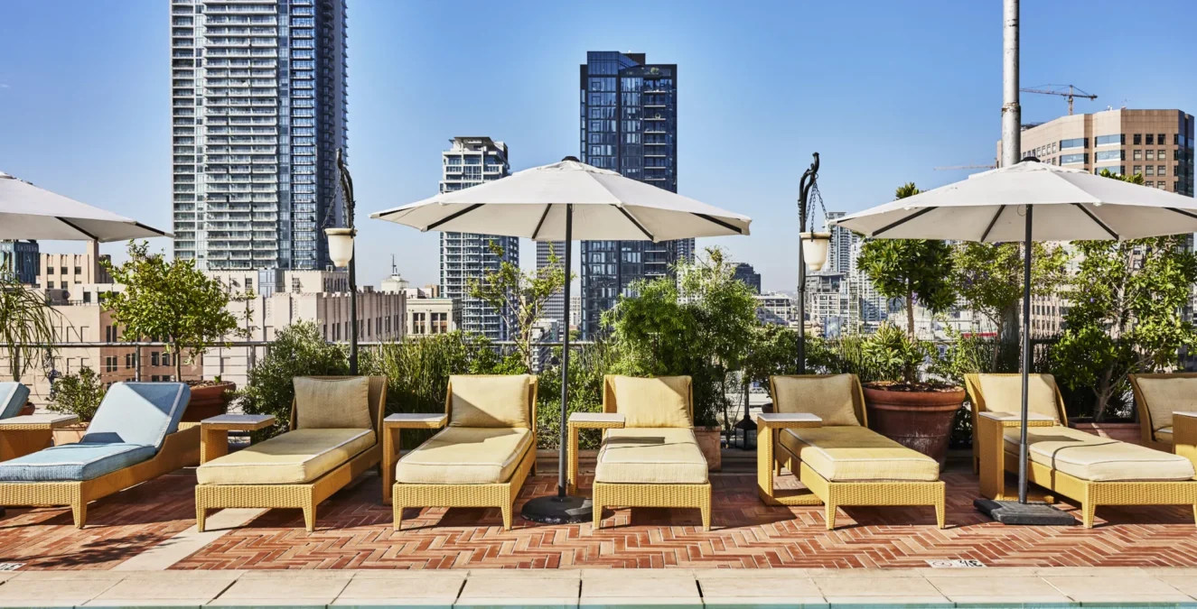Lounge chairs with umbrellas line the rooftop pool at Hotel Per La overlooking the downtown Los Angeles skyline.