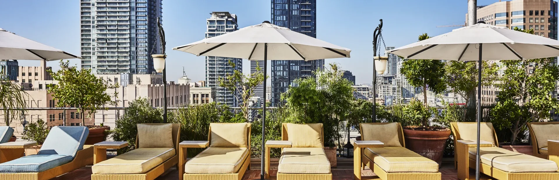 Lounge chairs with umbrellas line the rooftop pool at Hotel Per La overlooking the downtown Los Angeles skyline.