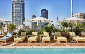 Lounge chairs with umbrellas line the rooftop pool at Hotel Per La overlooking the downtown Los Angeles skyline.