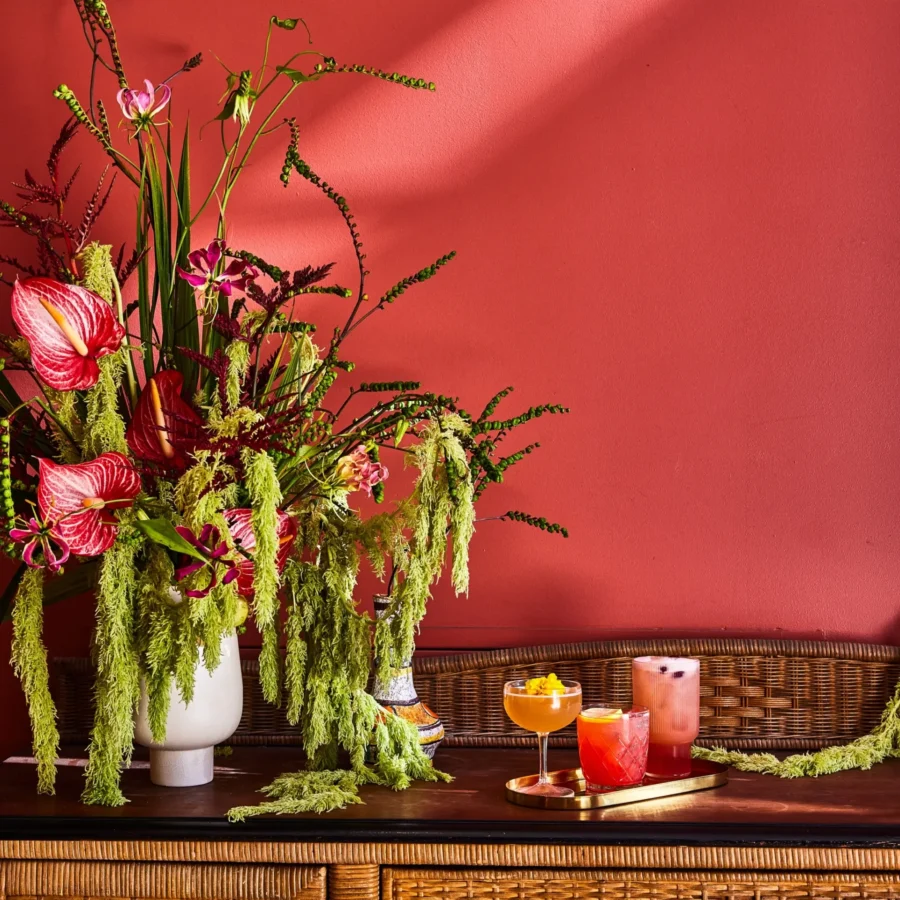 Artisan cocktails sit on a gold tray beside a tropical floral arrangement at Bar Clara rooftop bar in Los Angeles.