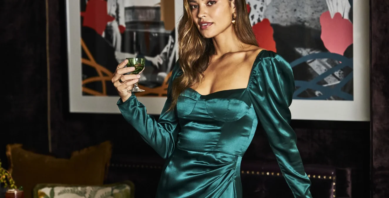 A woman in a green satin dress holds a cocktail in the stylish Bar Clara at our boutique hotel in downtown LA.