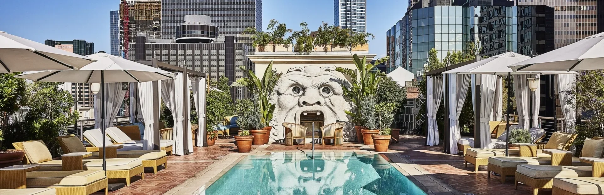 Relax at the Bar Clara rooftop pool, featuring elegant loungers and a stone sculpture in downtown Los Angeles.