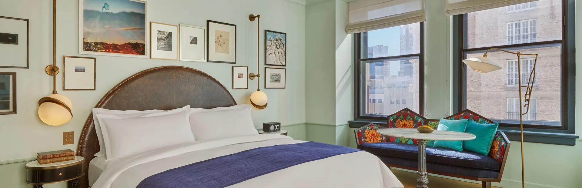Modern guest suite featuring a leather headboard, gallery wall, and window seating in a boutique Los Angeles hotel.