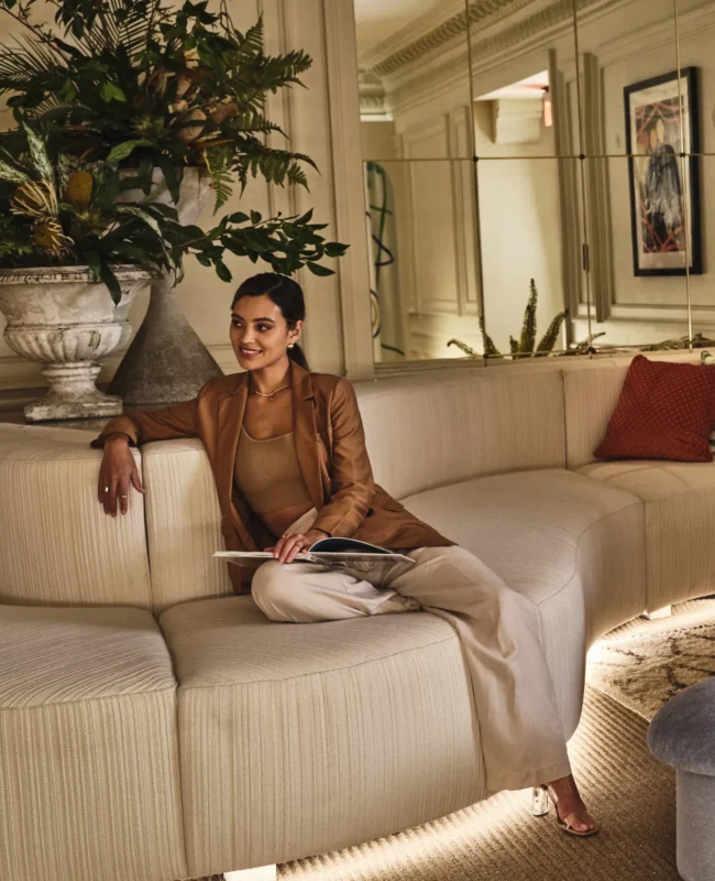 A guest relaxes on a stylish curved sofa in the elegant, plant-filled lobby lounge at Hotel Per La.