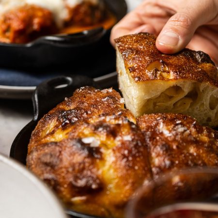 A guest enjoys salted focaccia bread at Ristorante Per L'Ora, a top choice among Italian restaurants in Los Angeles.