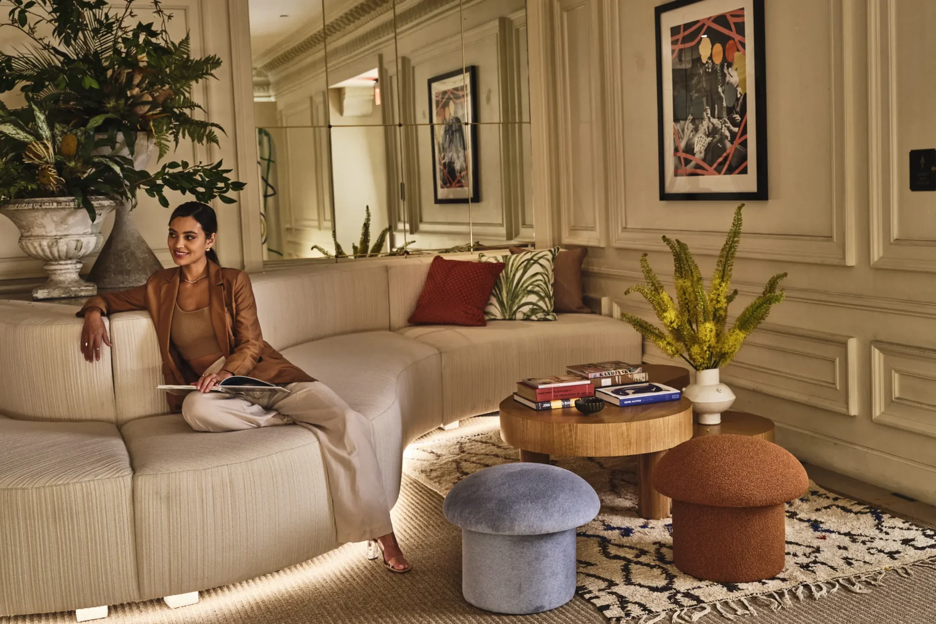 A guest relaxes on a curved sofa in a refined lounge at Hotel Per La featuring artistic decor and lush plants.