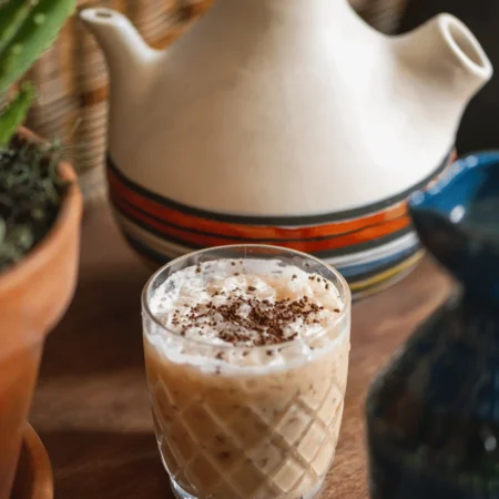 A chilled latte with foam and chocolate shavings in a crystal glass on a wooden table at Cafe Ora.