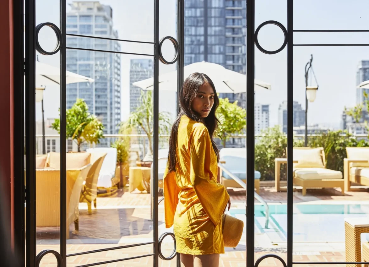 A guest in a yellow dress looks out toward the rooftop pool and city skyline at Bar Clara.
