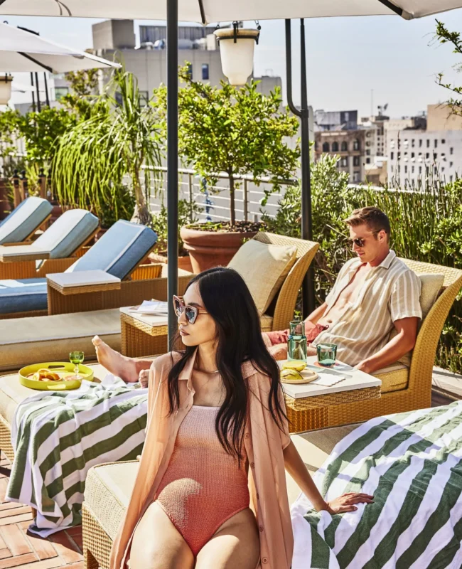 A woman in a pink swimsuit and a man relax on poolside loungers at the Bar Clara rooftop in Los Angeles.