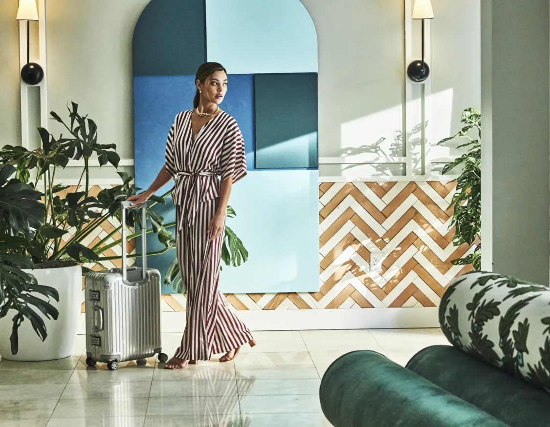 A stylish traveler with a silver suitcase walks through the art-filled, modern lobby of Hotel Per La.