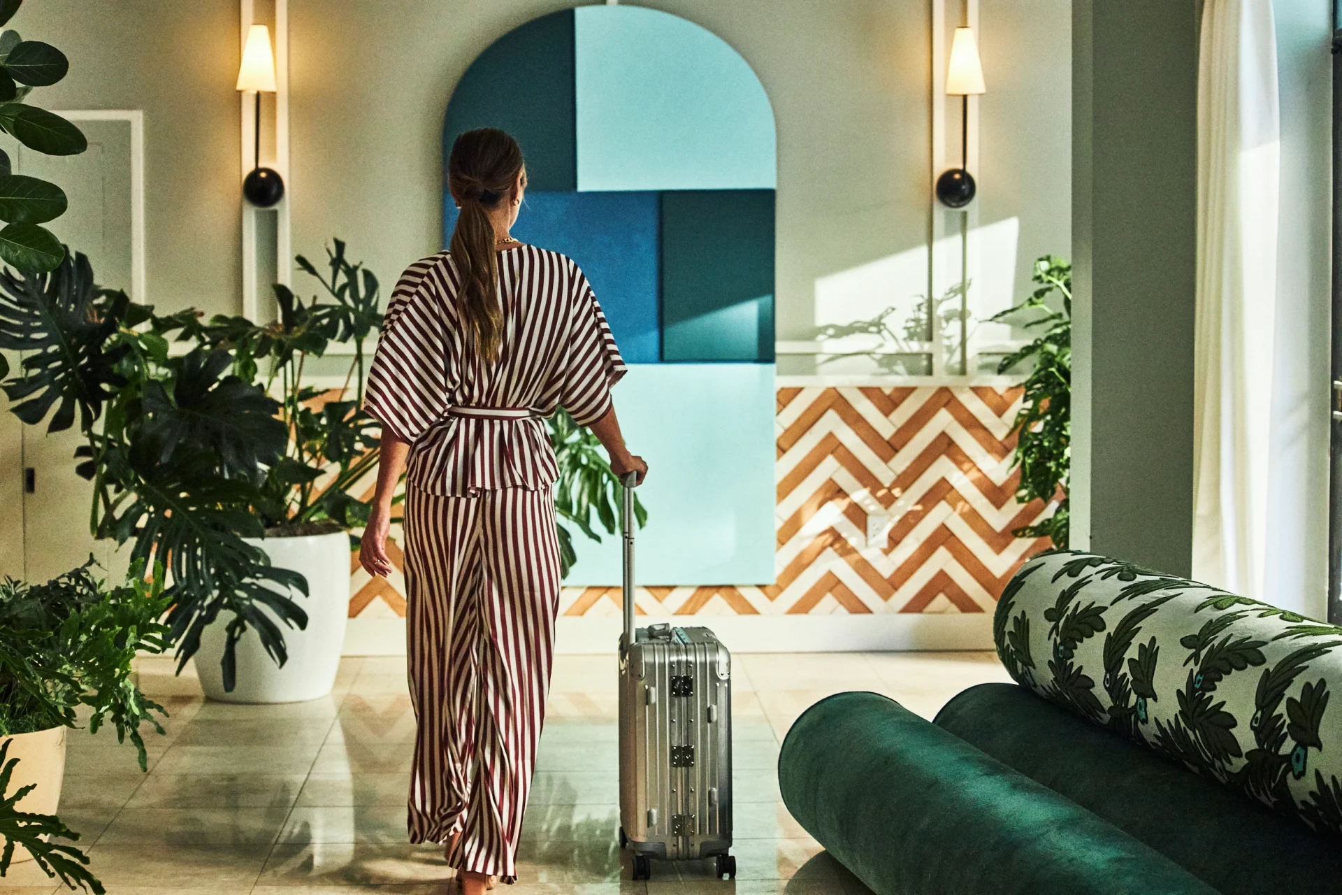 A guest in a striped outfit walks with her suitcase through the art-filled lobby at Hotel Per La.