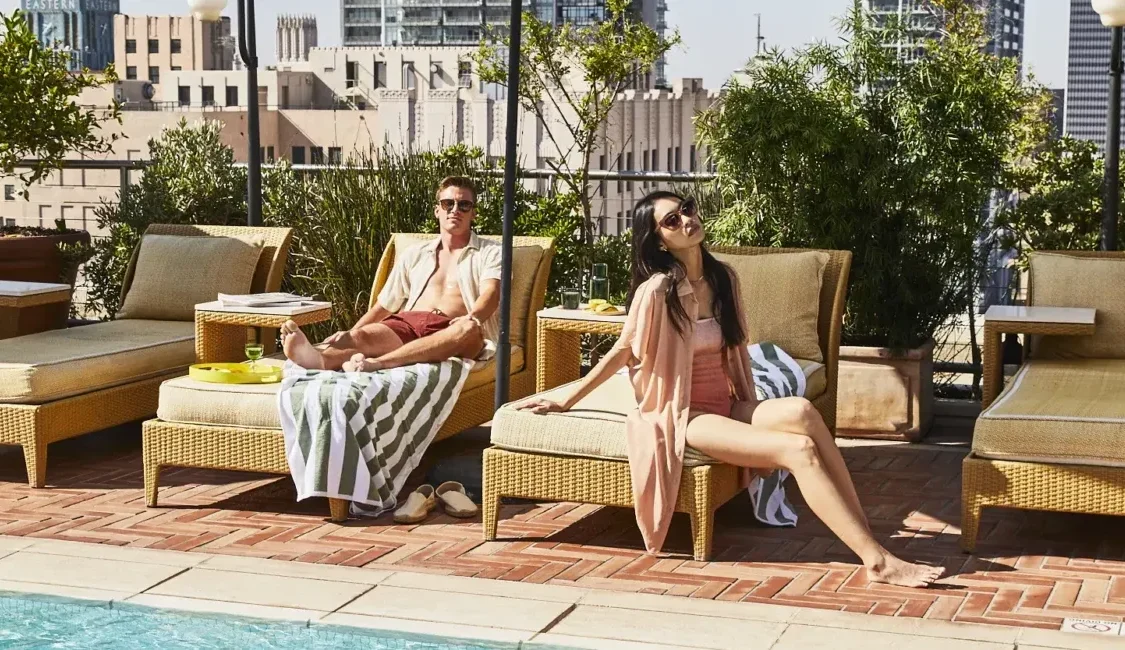 A man and woman relax on wicker lounge chairs by the rooftop pool at Bar Clara in downtown Los Angeles.