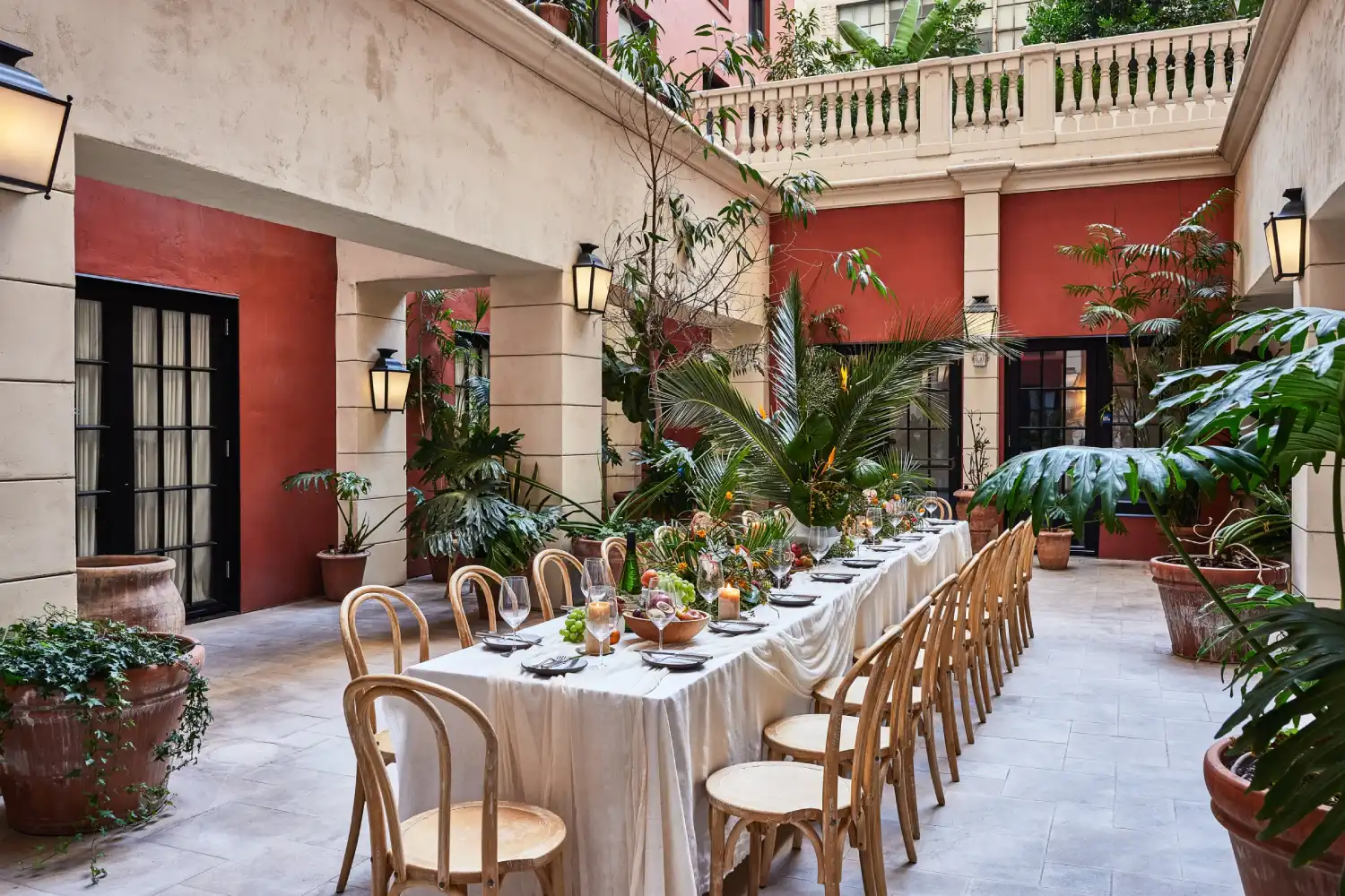 A long dining table set for an event in a Mediterranean-style courtyard with lush plants at Hotel Per La.