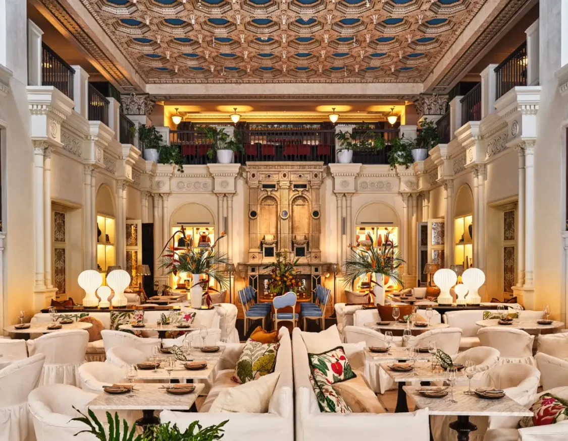 Ornate dining room at Ristorante Per L'Ora featuring white plush seating, marble tables, and a gold coffered ceiling.