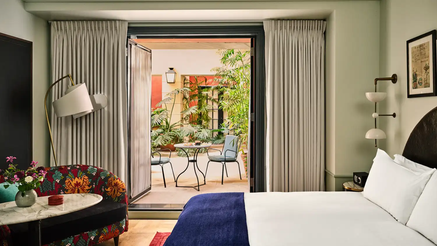 Sunlight fills a boutique hotel room in Los Angeles with an open door leading to a lush private courtyard terrace.