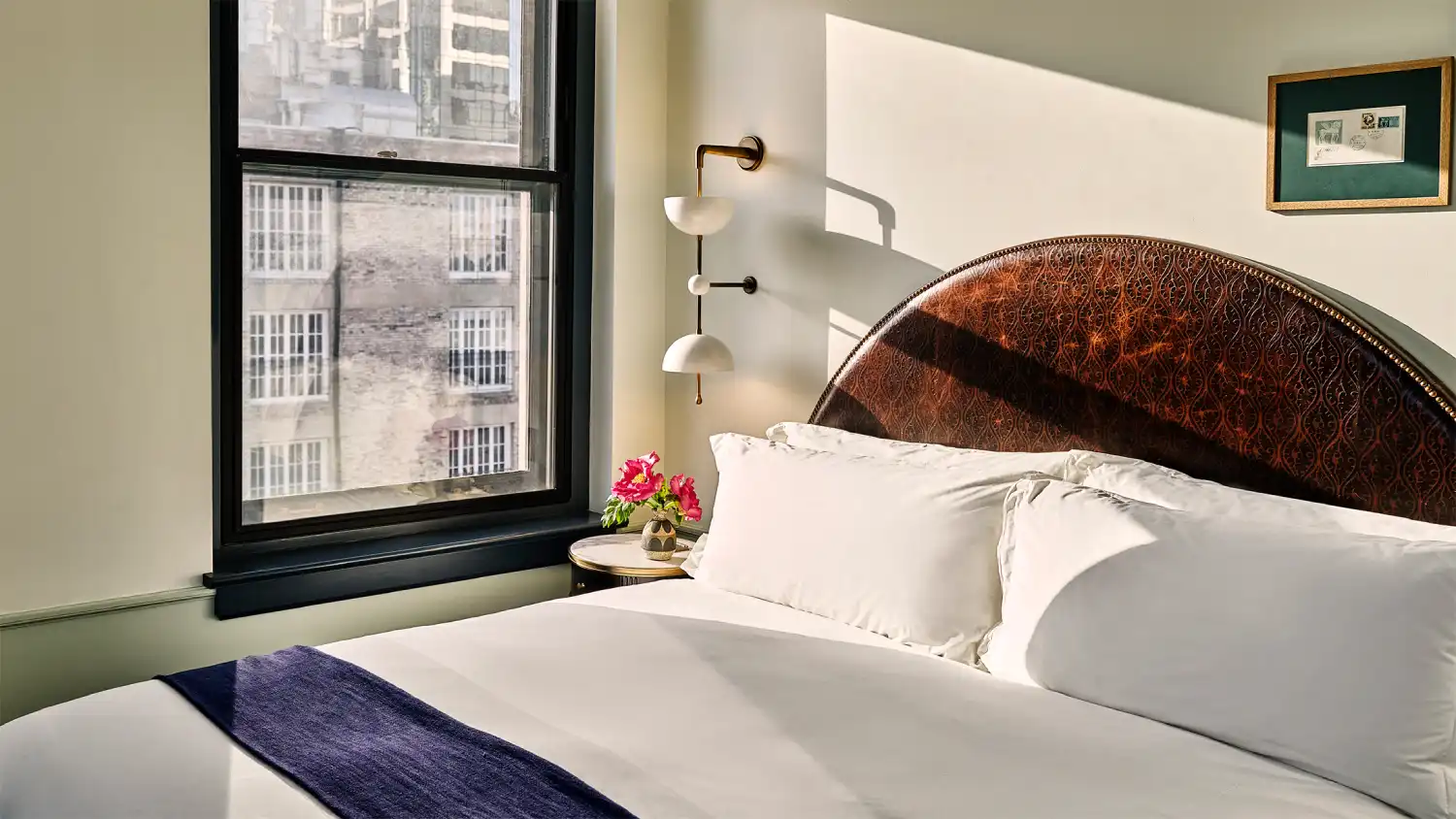 Morning light fills a guest room at Hotel Per La featuring a decorative headboard and views of downtown Los Angeles.