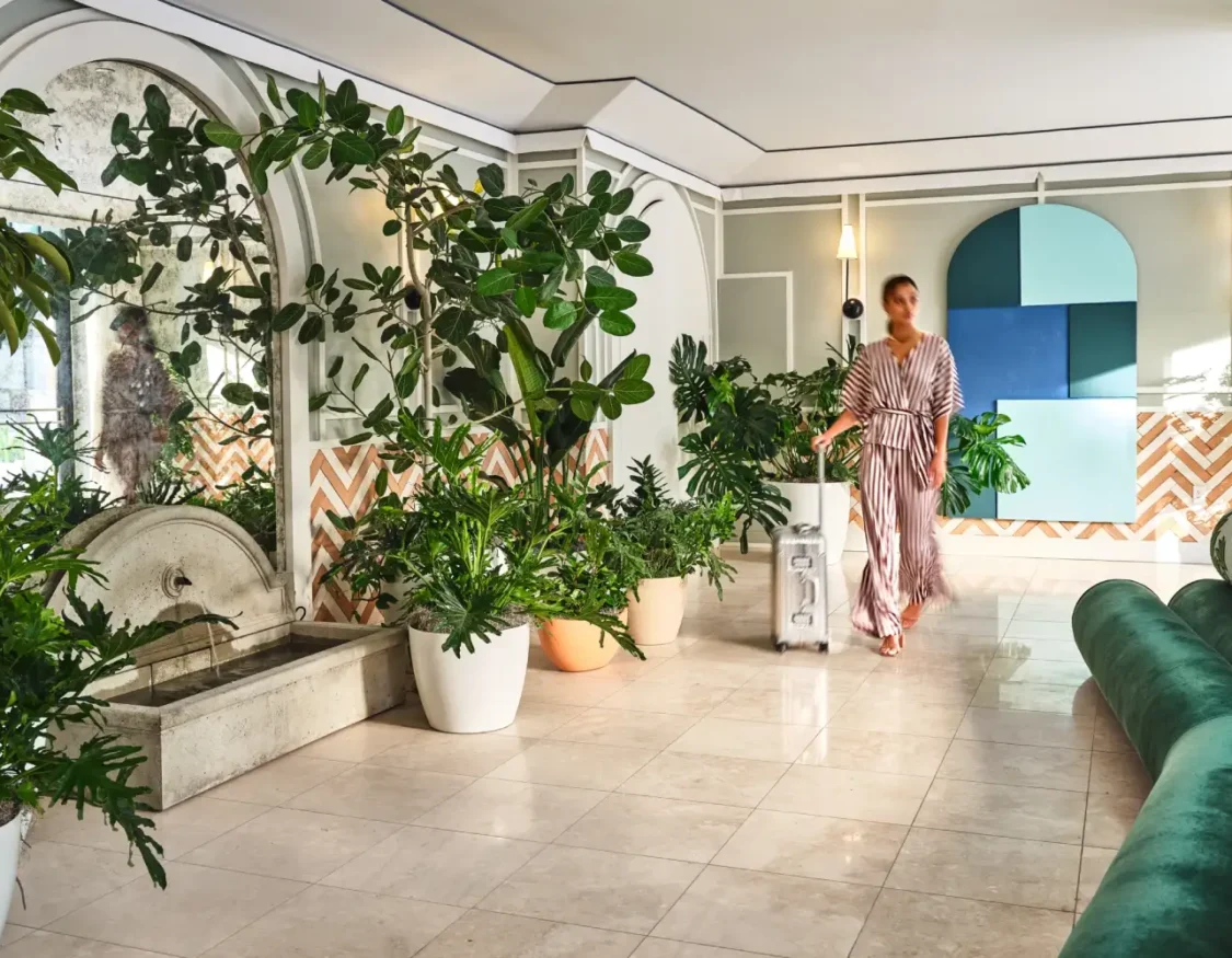A guest walks through the lush, plant-filled lobby of this boutique hotel in Los Angeles with their suitcase.