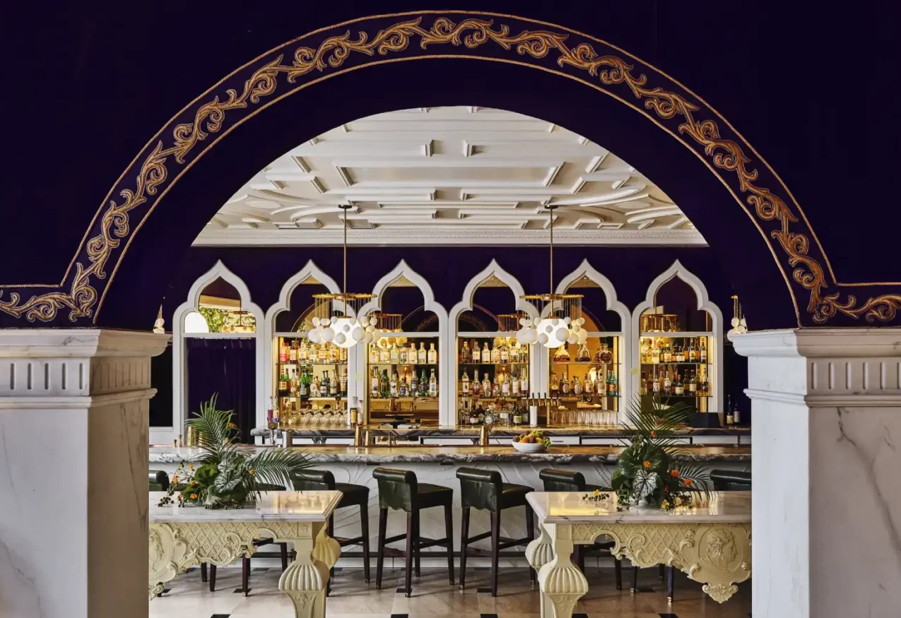 Gilded arches frame a marble bar with green stools at Ristorante Per L'Ora, a luxury Italian restaurant in Los Angeles.