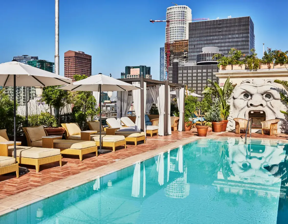 Guests enjoy the sunny rooftop pool and Bar Clara lounge surrounded by downtown Los Angeles skyscrapers.