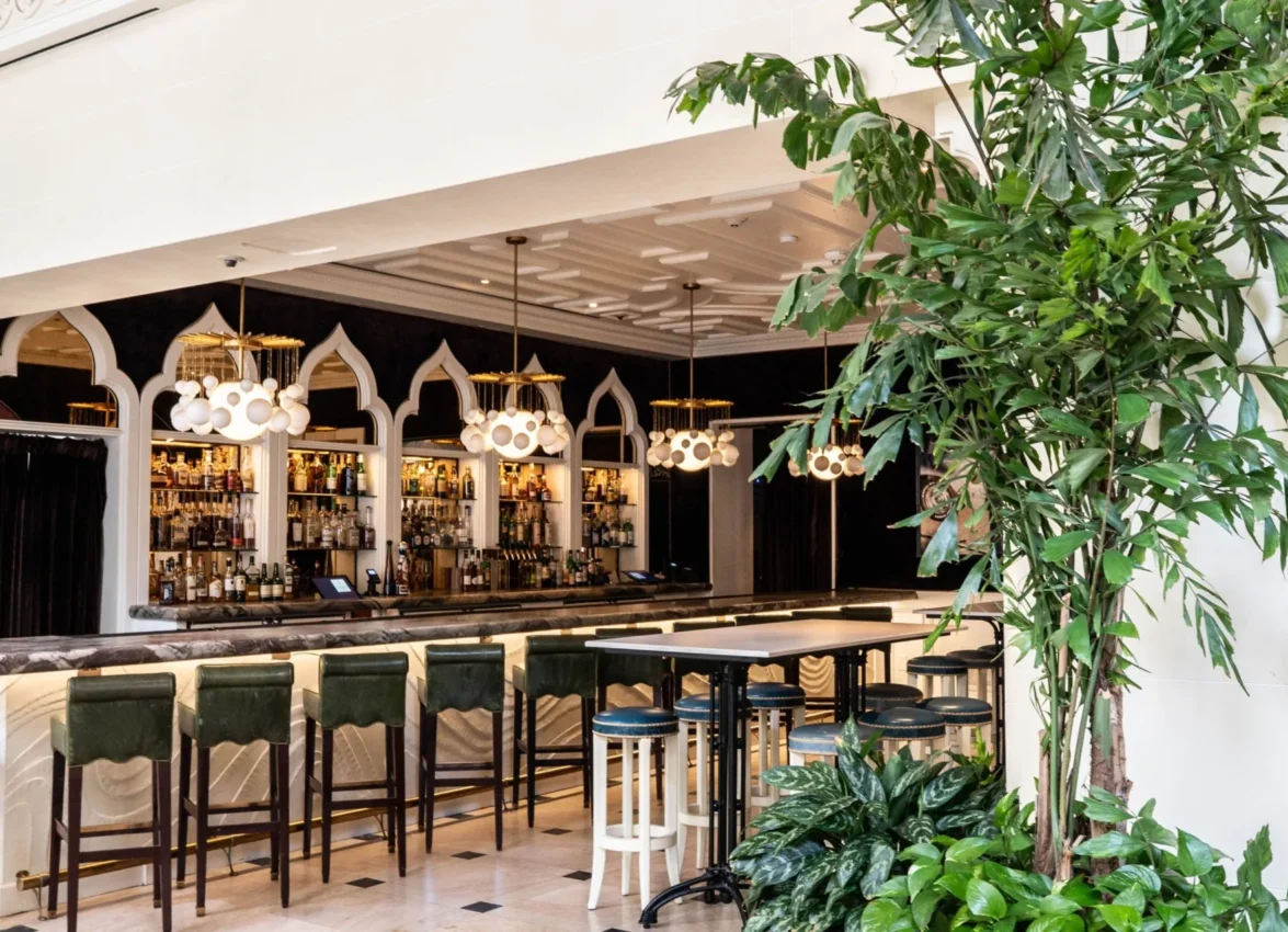Lush plants frame a stylish bar with green leather stools at Ristorante Per L'Ora, an Italian restaurant in LA.