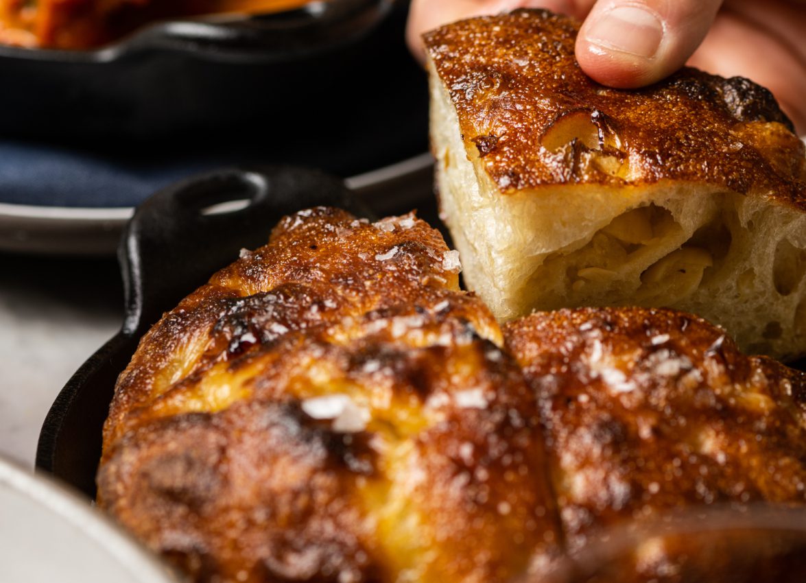 A hand picks up a piece of warm sea salt bread next to meatballs at an Italian restaurant in Los Angeles.