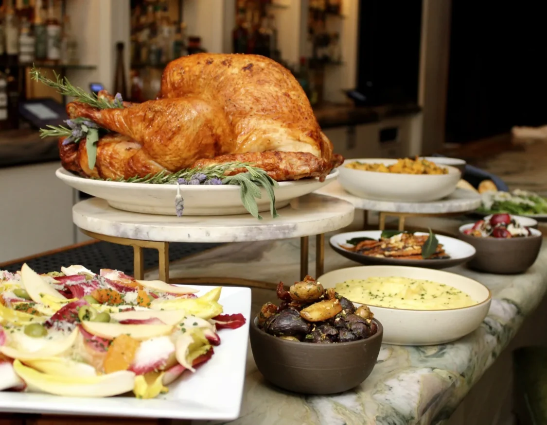 A roasted turkey garnished with herbs sits on a marble stand alongside seasonal side dishes at Ristorante Per L'Ora.