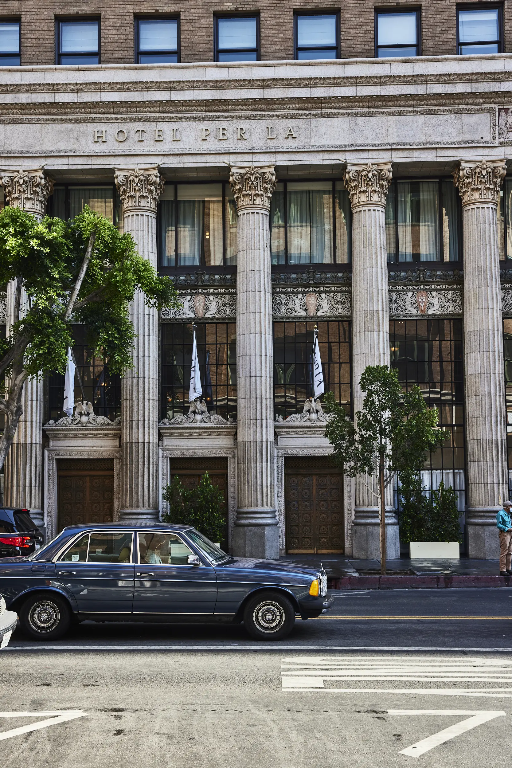 A vintage blue car parked in front of the grand stone columns at Hotel Per La in downtown Los Angeles.