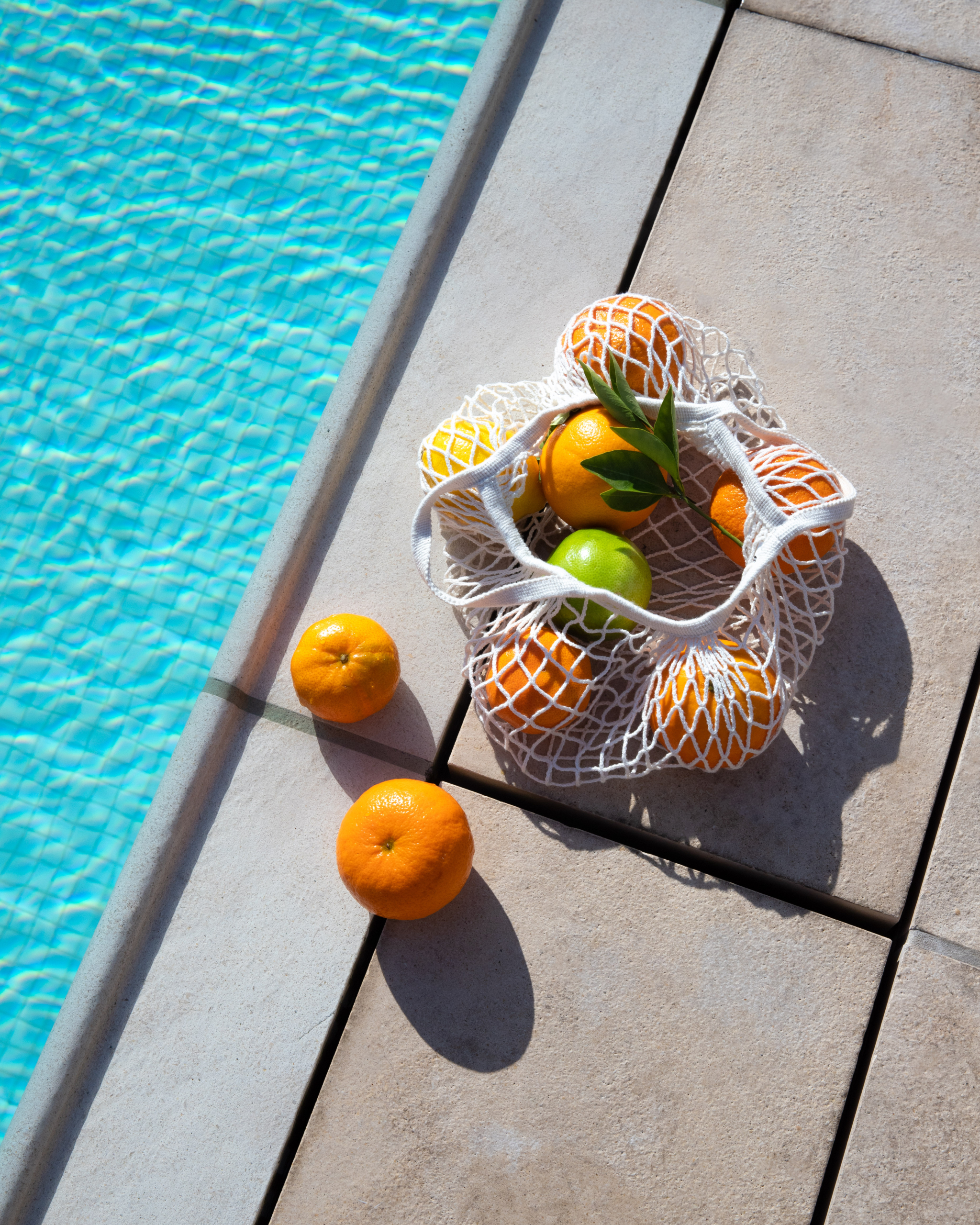 A mesh bag of oranges rests on the stone edge of the Bar Clara rooftop pool at Hotel Per La.