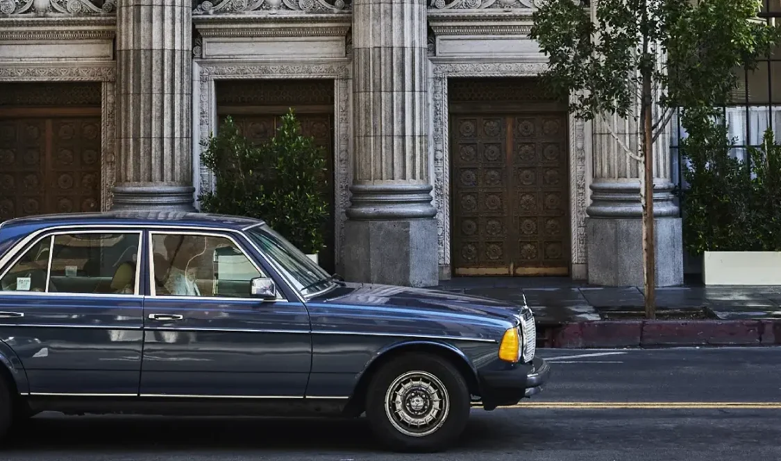 A classic blue car parked in front of the ornate stone columns of Hotel Per La in downtown Los Angeles.