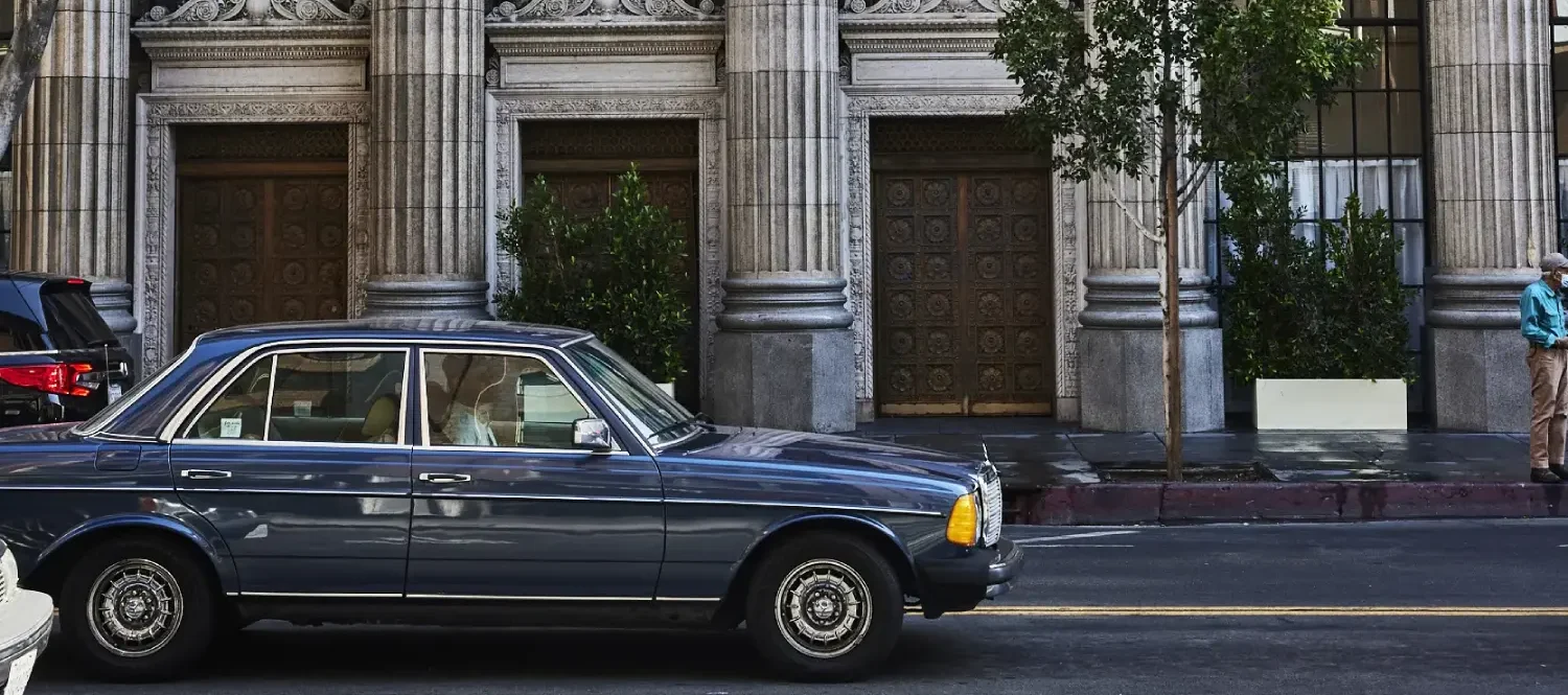 A classic blue car parked in front of the ornate stone columns of Hotel Per La in downtown Los Angeles.
