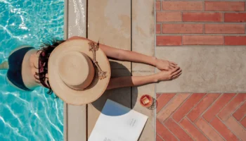 women in hat poolside with a book and drink,